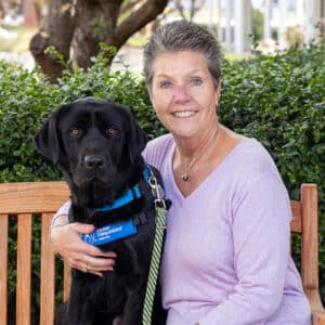 a smiling woman on a bench sitting next to a yellow lab service dog