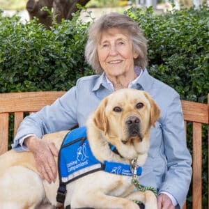 a smiling woman on a bench sitting next to a yellow lab service dog