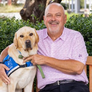 a smiling man sitting next to a yellow lab service dog