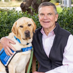 a smiling man sitting next to a yellow lab service dog