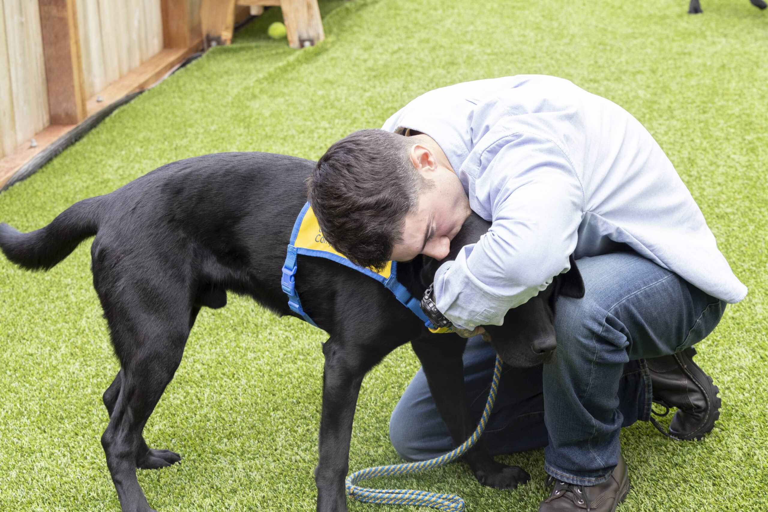 a puppy raiser kneels, hugging the black puppy he raised.