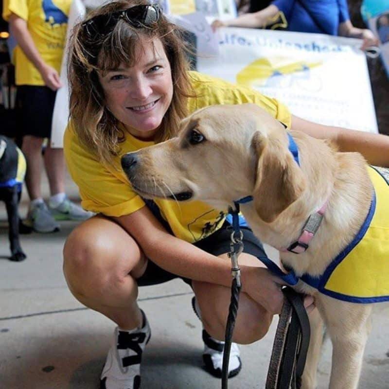 A smiling woman posing with a dog in a service vest