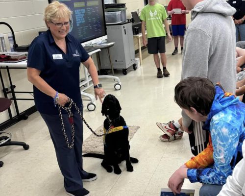 ffa_minicrop3 A woman demonstrating with a service dog to a group of seated students in a classroom.