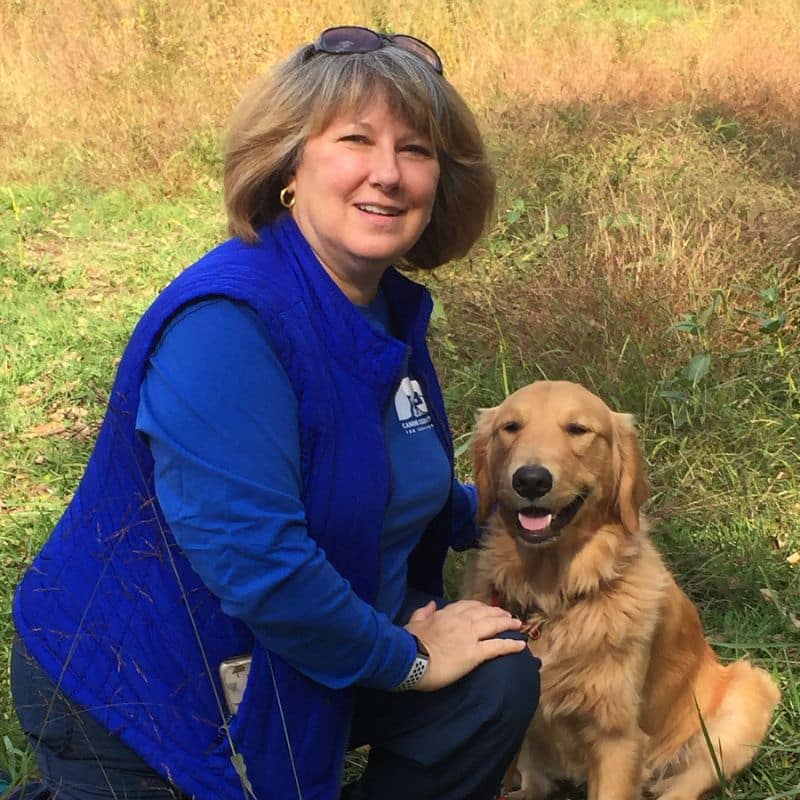 A smiling woman posing with a dog in a service vest