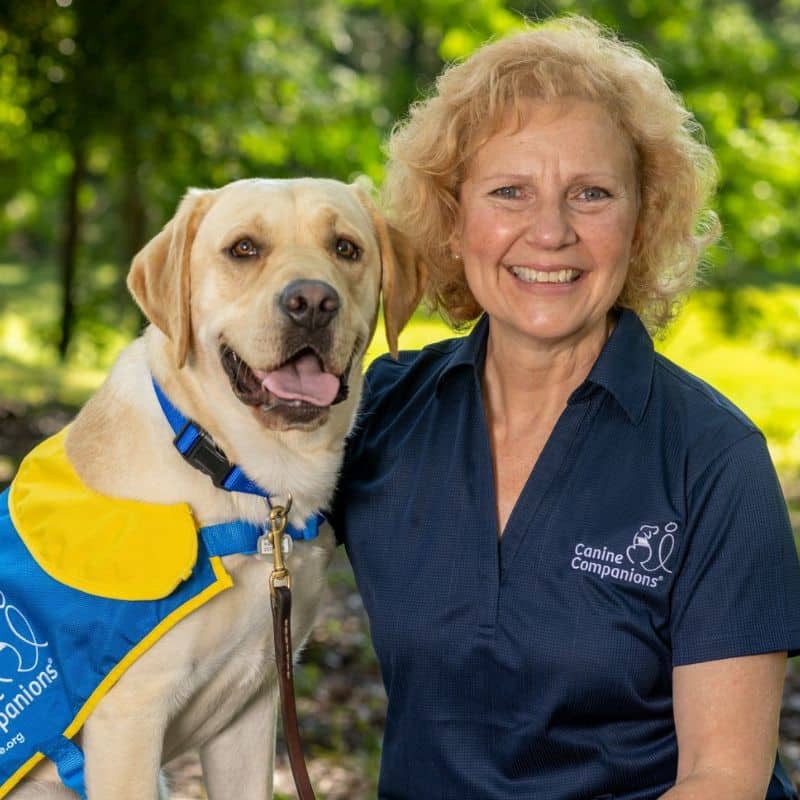 A smiling woman posing with a dog in a service vest