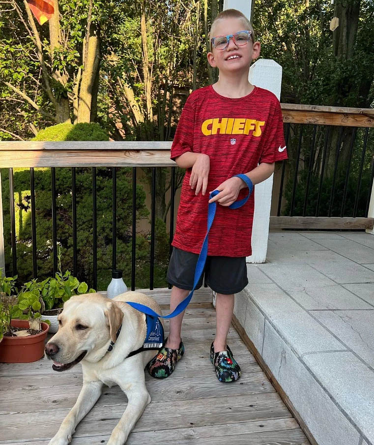 a young boy holds the leash of a yellow lab service dog