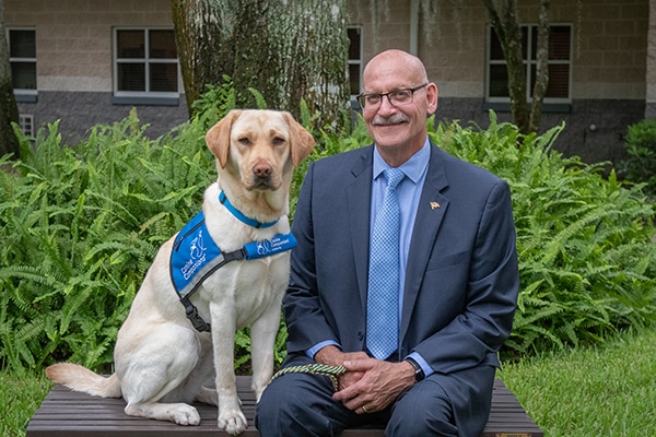 a man in a suit on a bench next to a canine companions dog