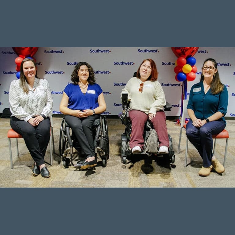 two women sitting in chairs and two women in wheelchairs, all sitting together with a backwall that has multiple small logos of Southwest and red, yellow and blue clusters of small balloons on each side