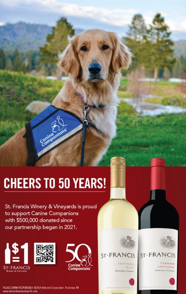 A golden retriever wearing a blue vest labeled 'Canine Companions' sits outdoors with a scenic background of trees and a body of water. The advertisement promotes St. Francis Winery & Vineyards' support for Canine Companions, highlighting a partnership with $500,000 donated since 2021, along with images of two wine bottles and a QR code.