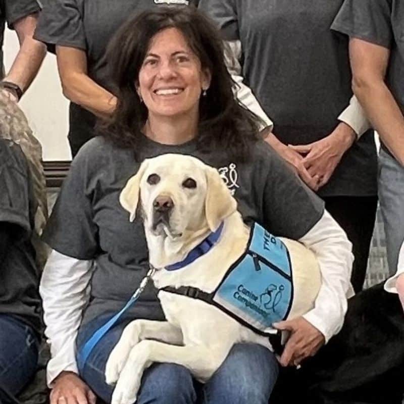 A smiling woman posing with a dog in a service vest