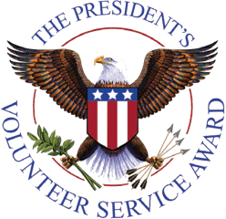 Emblem of The President's Volunteer Service Award featuring a bald eagle with outstretched wings, holding an olive branch and arrows, and a shield with red, white, and blue stripes and stars, encircled by the text 'THE PRESIDENT'S VOLUNTEER SERVICE AWARD.'